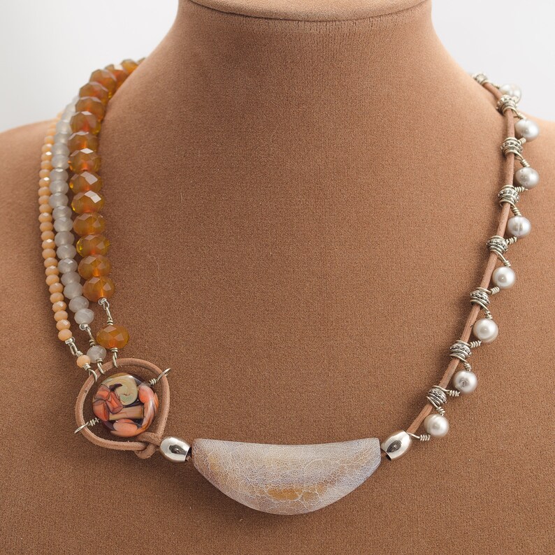 May include: A multi-strand necklace featuring brown, white and grey beads, a large grey and white pendant, and a smaller pendant with a colourful design.