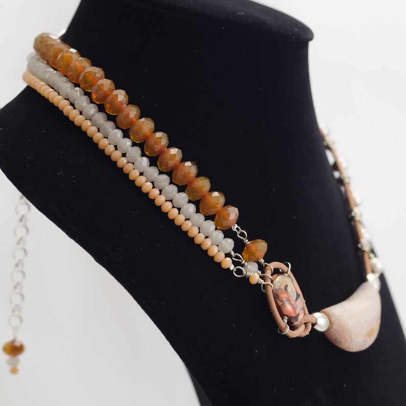 May include: A multi-strand necklace with brown, beige, and white beads. The necklace features a large, brown, and white stone pendant.