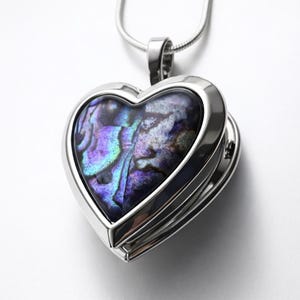 Op de afbeelding: Een hartvormige hangerketting met een zilverkleurig metalen frame. De hanger heeft een kleurrijke, iriserende abalone schelpinleg met tinten paars, blauw en groen. De ketting heeft een delicate ketting.