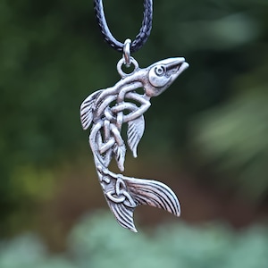 Peut inclure: Pendentif argenté en forme de poisson, orné de motifs de nœuds celtiques. Le poisson est suspendu à un cordon noir. Le pendentif présente des nageoires et une queue détaillées, avec une surface texturée.