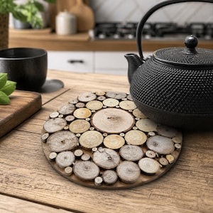 Puede incluir: Un salvamanteles redondo de madera hecho de pequeñas rodajas de madera natural dispuestas en un patrón de mosaico. Una tetera de hierro fundido negro descansa sobre el salvamanteles. El salvamanteles está sobre una mesa de madera en una cocina.