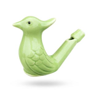 Può includere: Un fischietto in ceramica verde chiaro a forma di uccello con finitura lucida. Il fischietto presenta una forma aviaria stilizzata con becco appuntito, un piccolo occhio nero e dettagli delle ali modellati sul lato, con il bocchino sulla coda.