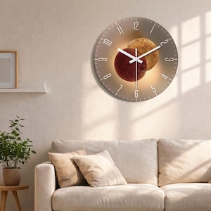 May include: A round wall clock with a space theme. The clock face is a light brown color with white numerals and hands. Two planets, one red and one gold, are in the center. The clock is hanging on a beige wall.