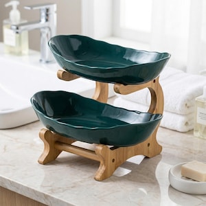 May include: A two-tiered serving tray featuring teal ceramic bowls and a natural bamboo frame. The bowls have a wavy edge design. The bamboo frame has a curved design and is supported by two legs. Ideal for displaying items in a bathroom or kitchen.