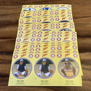 May include: A pile of yellow baseball cards featuring Gary Carter, a catcher. The cards have a circular design with a baseball and the word "Zellers" repeated across the top. The bottom cards have the text "Gary Carter" and "Catching Position".