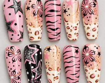 Könnte beinhalten: Ein Set aus zehn künstlichen Fingernägeln mit verschiedenen Designs, darunter schwarze Glitzersterne auf rosa und schwarzem Grund, rosa Tigerstreifen, Leopardenmuster und florale Motive, akzentuiert mit kleinen weißen Perlen in glänzender Optik.