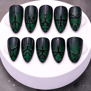 May include: A set of ten dark green, almond-shaped false nails. Each nail features a black, geometric design. The nails are arranged on a white, circular display, showcasing the intricate patterns and glossy finish.