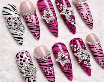May include: A set of ten long, pointed artificial nails. Designs include zebra stripes, leopard spots, and tiger stripes in black, white, and pink. Some nails feature rhinestone star and gem embellishments, and others have a nude-colored base with a rhinestone border.