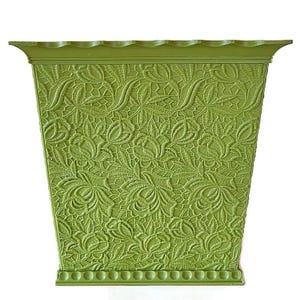 May include: A green square planter with an embossed floral design. The planter has a scalloped top edge and a decorative base. The detailed pattern features flowers and leaves, creating a textured surface. The planter is made of a solid, durable material.