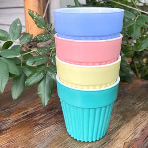 May include: A stack of four cylindrical bowls in pastel colours, including light blue, soft pink, pale yellow, and bright turquoise. Each bowl features a smooth upper rim and a vertically ribbed lower section, creating a uniform, layered appearance.
