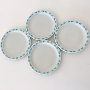 May include: Four white ceramic plates with a teal leaf pattern border. The plates are round and have a simple, clean design. The teal leaf pattern adds a touch of color and visual interest to the plates.