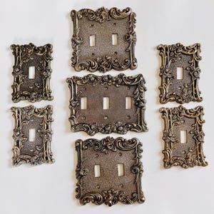 Puede incluir: Cubiertas de interruptores de luz de estilo antiguo en bronce. Las cubiertas presentan intrincados diseños florales y de volutas. El conjunto incluye placas de interruptor individuales, dobles y triples, añadiendo un toque vintage.