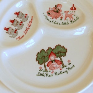 May include: A white ceramic divided plate with three sections. Each section features a different nursery rhyme illustration: "Three Little Kittens", "Mary Had a Little Lamb", and "Little Red Riding Hood".