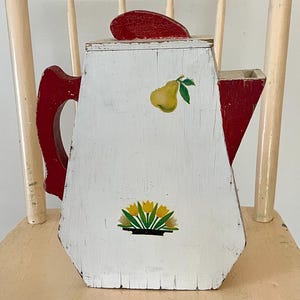 May include: A white wooden teapot with a red lid and handle. The teapot is decorated with painted yellow pears and yellow flowers.