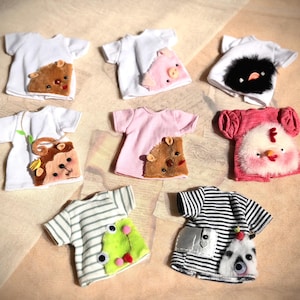May include: A selection of small t-shirts in different colours, each decorated with a unique animal or character design. The shirts feature a variety of creatures, including a bear, pig, panda, and chicken, with details like fur and stripes.