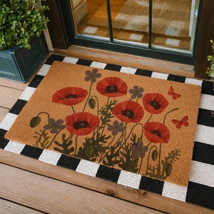 May include: A rectangular doormat with a brown background features a floral design of red poppies and butterflies. The mat is bordered by a black and white checkered pattern, and is placed in front of a glass door.