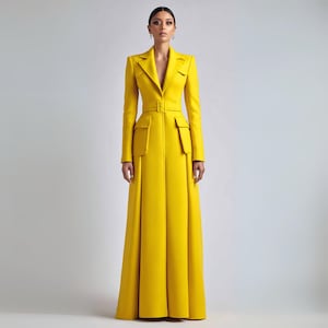 May include: A long, bright yellow coat with a tailored design. The coat features a notched collar, long sleeves, a belted waist, and two front pockets. The skirt portion of the coat is pleated, creating a flowing silhouette.