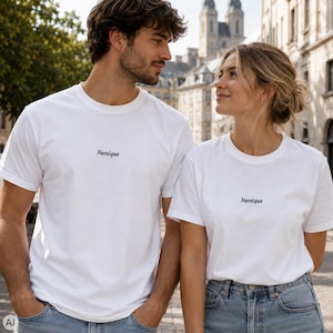 Könnte beinhalten: Zwei weiße kurzärmelige T-Shirts mit Rundhalsausschnitt und dem Wort "Herzique", das in einer kleinen, dunklen Schreibschrift mittig auf der Brust aufgedruckt ist. Die T-Shirts bestehen aus schlichtem weißem Stoff und werden zu blauen Jeans getragen.