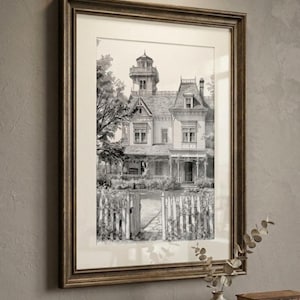 Op de afbeelding: Een ingelijste zwart-wit inkttekening van een Victoriaans huis met een toren, een veranda rondom en een houten hek. Het kunstwerk zit in een donkerbruine houten lijst met een crèmekleurige passe-partout aan een muur met textuur.
