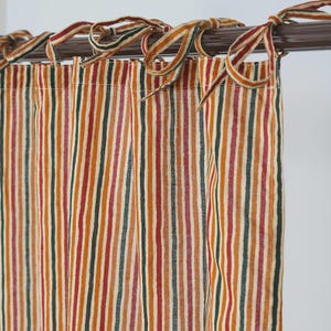 May include: A curtain panel featuring vertical stripes in shades of orange, dark green, red, and cream. The fabric is attached to a dark brown curtain rod using integrated fabric ties that are knotted at the top, creating a gathered, pleated effect.