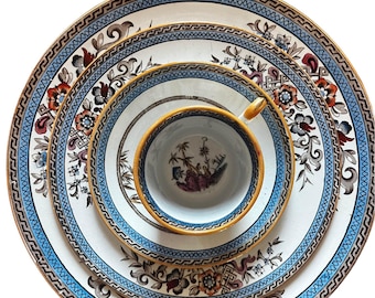 Könnte beinhalten: Ein Set aus vier weißen Porzellantellern mit blauen und goldenen Rändern und floralen Mustern. Die Teller sind übereinander gestapelt, in der Mitte befindet sich eine kleine weiße Porzellantasse.
