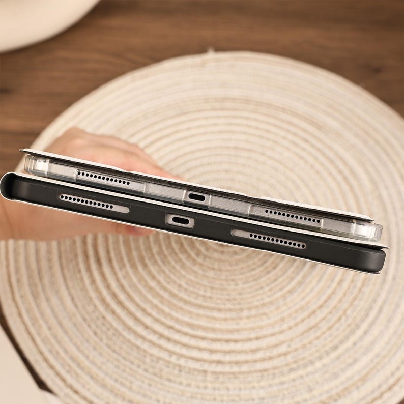 May include: A tablet device encased in a protective cover, featuring a black frame with visible speaker grilles and a central charging port. The device is positioned to show the side profile, highlighting the precise cutouts for hardware access.