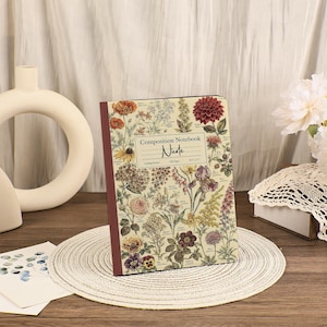 May include: A composition notebook with a cream-colored cover featuring a detailed botanical print of various flowers and plants in shades of red, yellow, and green. The center label reads Composition Notebook, Nicole, College Ruled, 100 Pages, 8.5 x 11.
