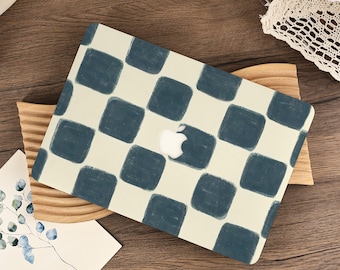 Könnte beinhalten: Eine Laptop-Hülle mit einem sich wiederholenden Muster aus dunkelblauen, abgerundeten Quadraten auf cremefarbenem Hintergrund. Das Design enthält einen mittigen Ausschnitt, der das weiße Apple-Logo freilässt. Die Hülle bedeckt den Laptop-Deckel und zeigt eine gitterartige Anordnung der blauen Formen auf dem hellen Untergrund.