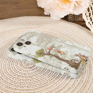 May include: Two phone cases stacked on top of each other. The cases have a light gray background with a tree design and a cartoon illustration of Winnie the Pooh and friends. The cases are on a woven mat.