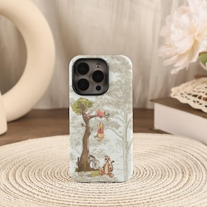 May include: A phone case featuring a whimsical illustration of Winnie the Pooh and friends. The design includes Pooh Bear hanging from a tree with a red balloon, with Tigger and Eeyore nearby. The case has a light background.