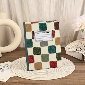Puede incluir: Un cuaderno de composición con una cubierta color crema con un patrón de cuadrados coloridos en rojo, verde, marrón y gris. El libro tiene una etiqueta blanca que dice "COMPOSITION BOOK". El lomo es de color verde azulado oscuro.