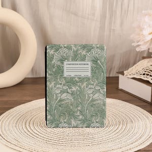 May include: A composition notebook with a green floral pattern. The cover features a repeating design of stylized flowers and leaves in shades of green. The notebook has a white label that reads "COMPOSITION NOTEBOOK".