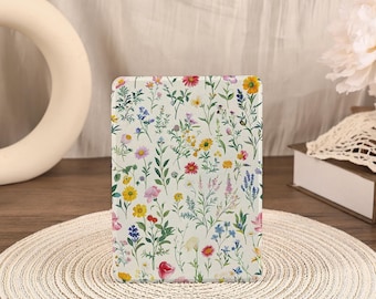 May include: A rectangular e-reader case featuring a white background covered in a colorful botanical pattern of various wildflowers, including yellow, pink, red, and blue blossoms with green stems and leaves, arranged in a dense, repeating floral design.