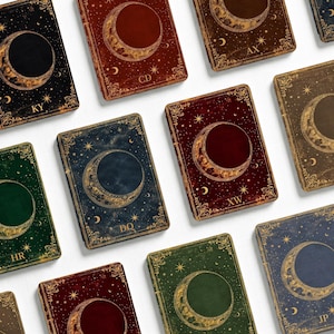 May include: A collection of rectangular notebooks featuring celestial designs with crescent moons, stars, and ornate gold-toned borders. Each cover displays a unique color, including deep red, forest green, navy blue, and black, with two-letter codes.