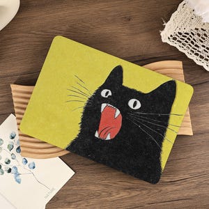 Peut inclure: Un set de table rectangulaire avec un fond jaune chartreuse vif et un grand motif central représentant un chat noir aux grands yeux blancs, la gueule ouverte révélant des détails intérieurs rouges, des dents blanches et une langue rose.