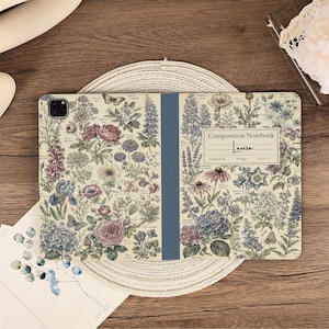 May include: A tablet case featuring a vintage-style botanical print with various flowers, leaves, and butterflies on a cream background. A central blue spine divides the design. A white label reads Composition Notebook, Lauren, 120 Pages, 8.5 x 11.