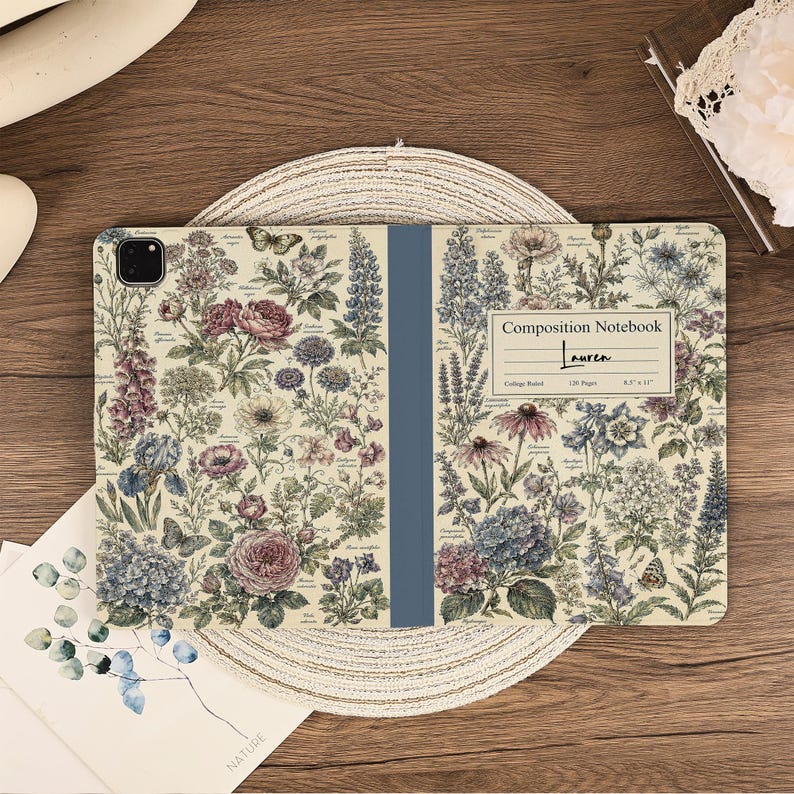 May include: A tablet case featuring a vintage-style botanical print with various flowers, leaves, and butterflies on a cream background. A central blue spine divides the design. A white label reads Composition Notebook, Lauren, 120 Pages, 8.5 x 11.