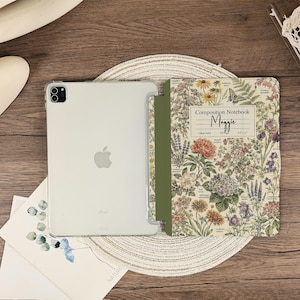 May include: A silver tablet in a clear case attached to a folding cover featuring a vintage-style botanical print with various flowers, a butterfly, and the text Composition Notebook Maggie College Ruled 100 Pages 8.5 x 11 inches.
