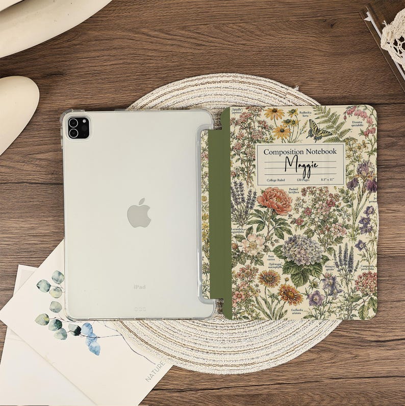 May include: A silver tablet in a clear case attached to a folding cover featuring a vintage-style botanical print with various flowers, a butterfly, and the text Composition Notebook Maggie College Ruled 100 Pages 8.5 x 11 inches.