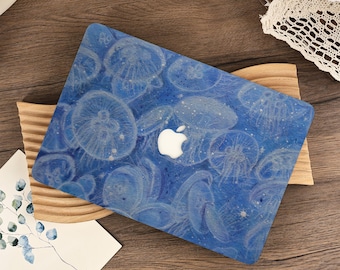 May include: A blue laptop case featuring a pattern of white jellyfish. The case has a white Apple logo and is resting on a wooden stand. The background includes a wooden surface and a card with the word "NATURE".