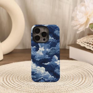 May include: A rectangular smartphone case featuring a dark blue night sky pattern with white, painterly clouds and small scattered white dots representing stars. The case has a large circular cutout at the top for the camera lens array.