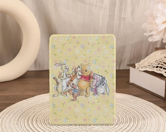 May include: A rectangular protective case for an electronic device featuring a light yellow background with a repeating pattern of small white, blue, and pink flowers. The centre displays a colourful illustration of Winnie the Pooh and friends.