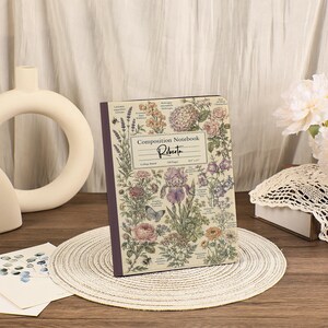 May include: A composition notebook with a cream-colored cover featuring a botanical illustration of various flowers, plants, and a butterfly. The text reads Composition Notebook, Roberta, College Ruled, 128 Pages, and 8.5 x 11 inches.