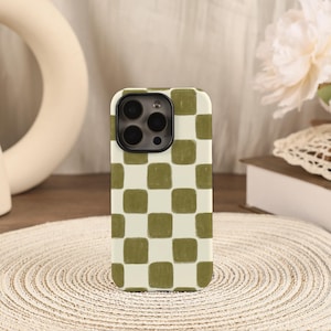 May include: A smartphone case featuring a repeating checkerboard pattern of muted olive green squares alternating with off-white squares. The case has a rectangular shape with rounded corners and a cutout for a triple-lens camera system.