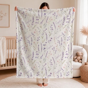 May include: A soft, off-white fleece blanket featuring a repeating watercolor pattern of purple lavender sprigs, small pink flowers, and green foliage, interspersed with the name Sophia written in a cursive, dark purple script font.