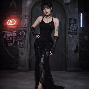 May include: A black halter dress with a lace overlay and a high slit. The dress features decorative metal studs and a flowing skirt. The model is wearing matching lace gloves and a choker necklace. The background includes brick and posters.