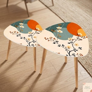 May include: Two small, triangular side tables with a floral design. The tabletop features a cream background with a stylized floral and branch pattern, and a teal and orange geometric design. The tables have light wood legs.