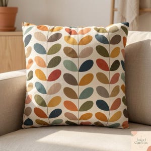 May include: Square throw pillow with a cream background and a repeating pattern of colorful leaf shapes in orange, yellow, brown, green, and blue. The pillow is on a beige sofa.