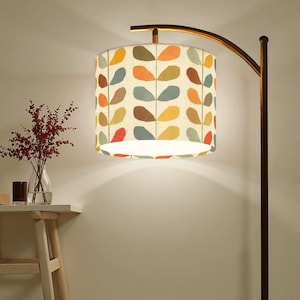 May include: A floor lamp with a cream-colored lampshade featuring a repeating pattern of colorful leaf shapes in red, orange, yellow, brown, and blue. The lamp has a curved, gold-toned arm and a dark brown pole.