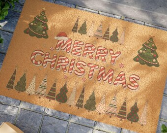 May include: A rectangular doormat with a tan background and a festive Christmas theme. The words "MERRY CHRISTMAS" are in red and white candy cane-striped letters. The mat is decorated with Christmas trees and a Santa hat.